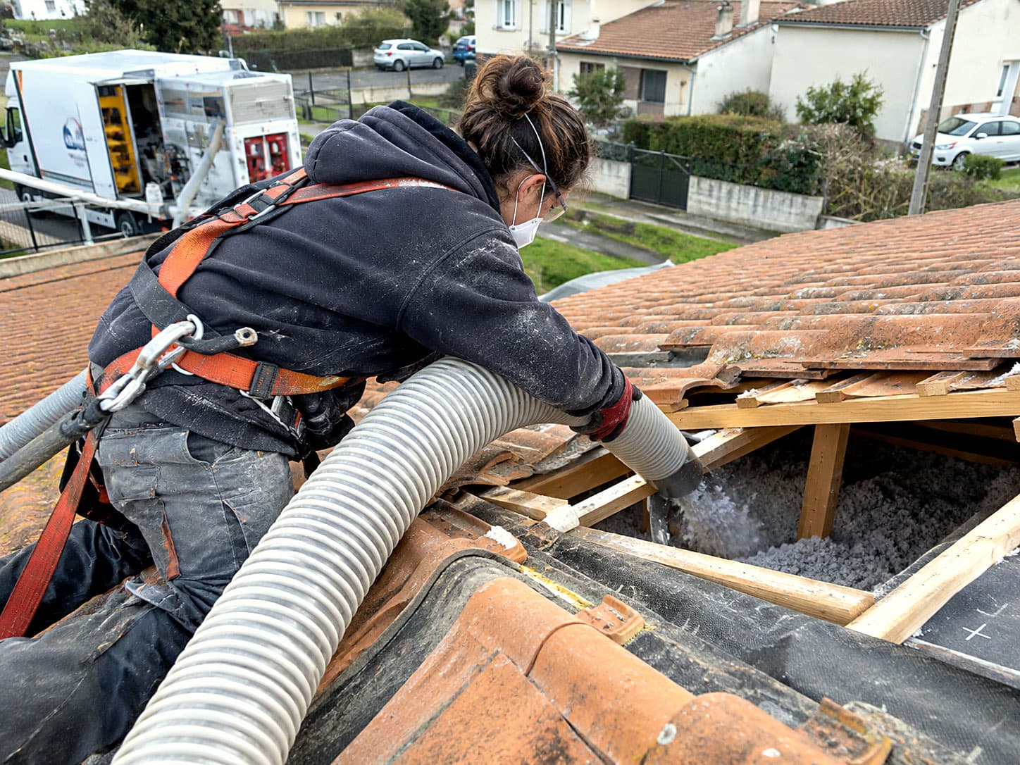 Une technicienne harnachée passe le tuyau de soufflage par une ouverture de la toiture.